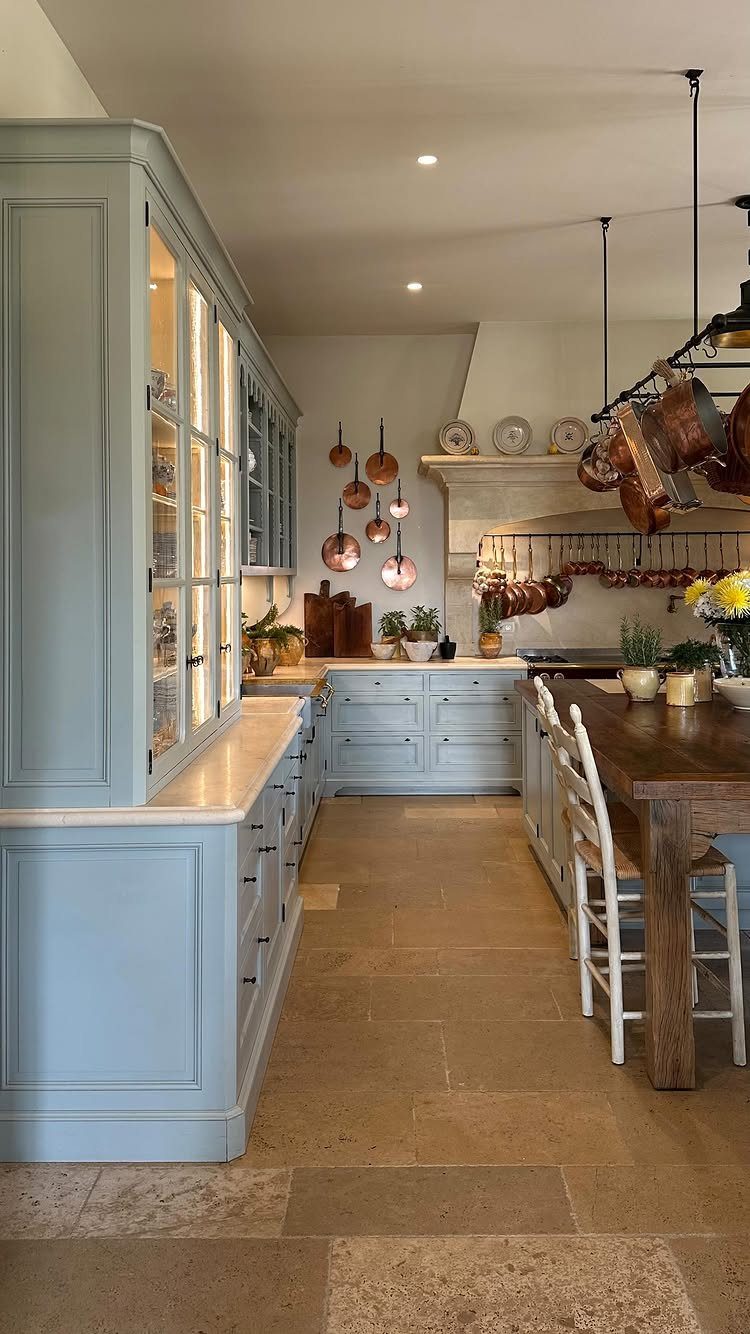 Rustic kitchen with light blue cabinets and copper pots hanging from the ceiling.