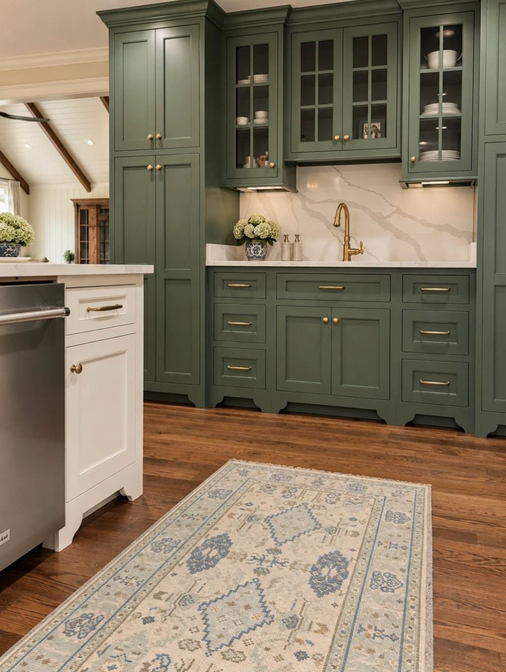 Sage green kitchen cabinets with gold hardware and white marble backsplash on wood floors