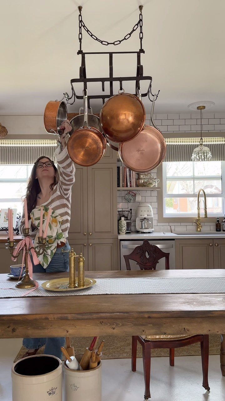 Woman reaching for copper pots hanging from a black metal ceiling pot rack.