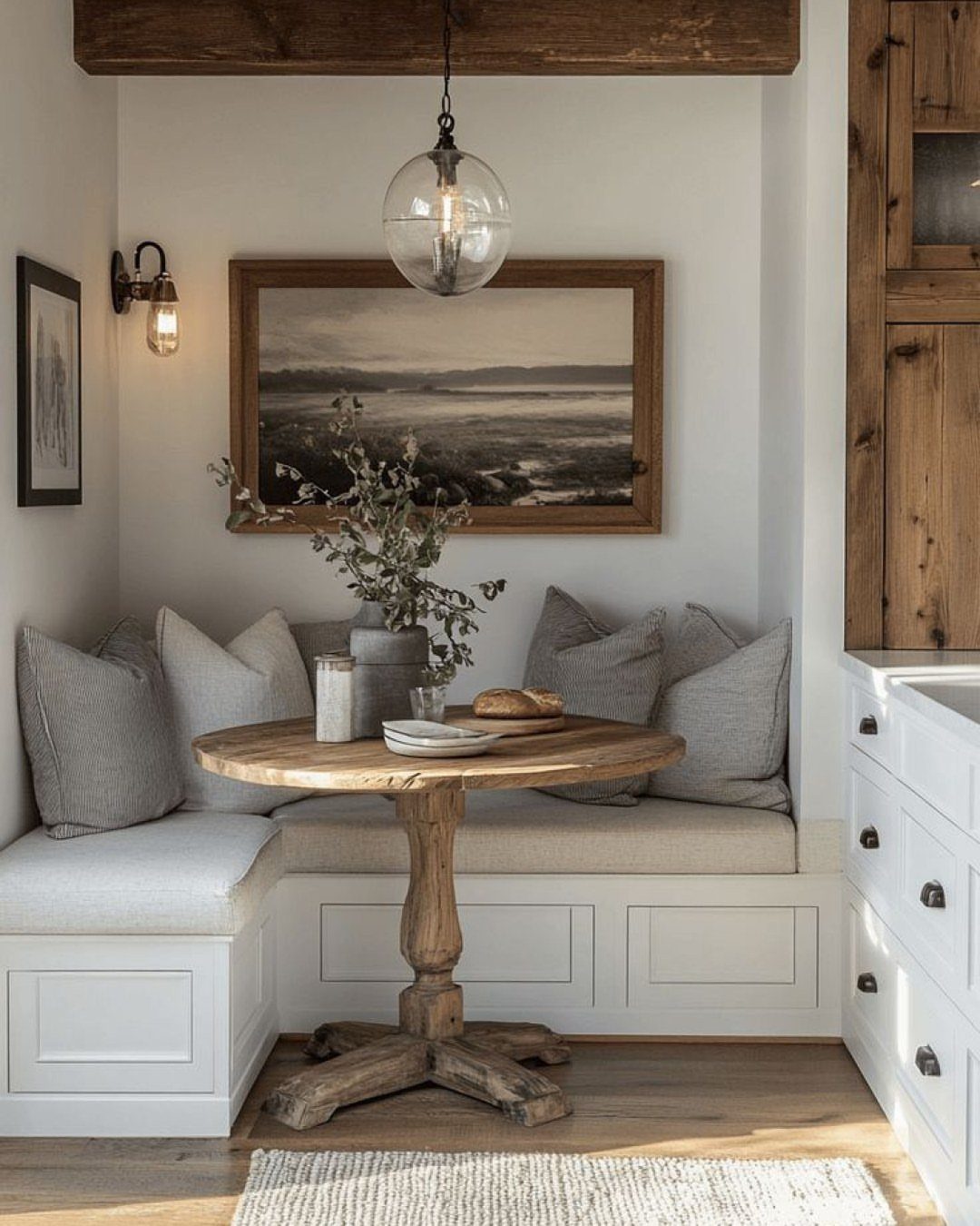 Round wooden pedestal table with a white built-in bench and grey cushions.