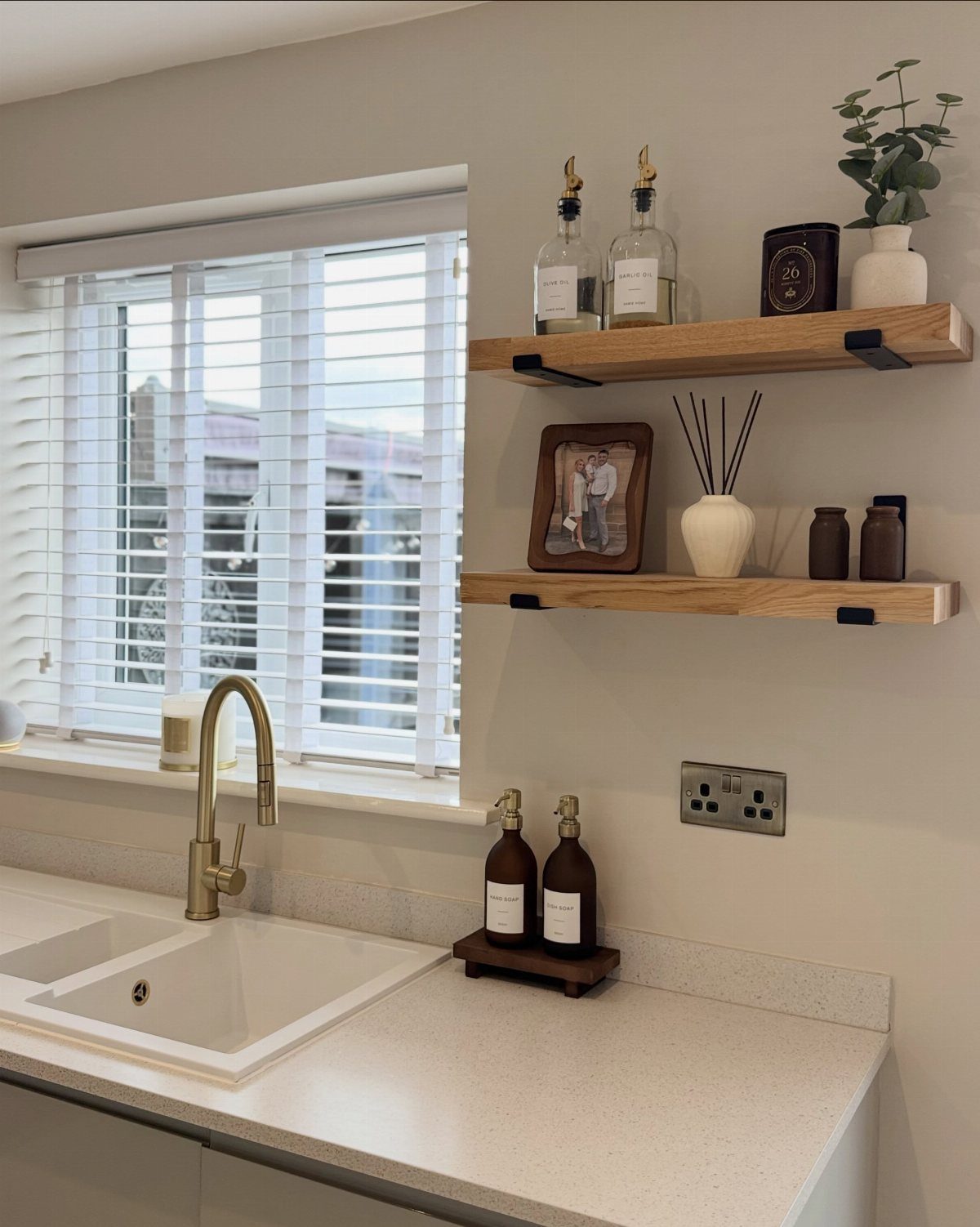 White kitchen sink and gold faucet with floating natural wood shelves and decor.