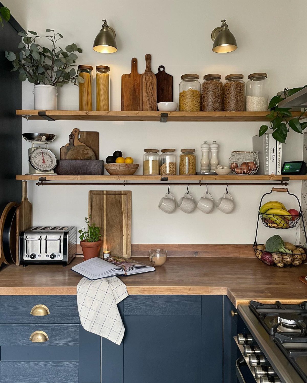 Wooden open shelves holding glass jars and cutting boards above blue kitchen cabinets.
