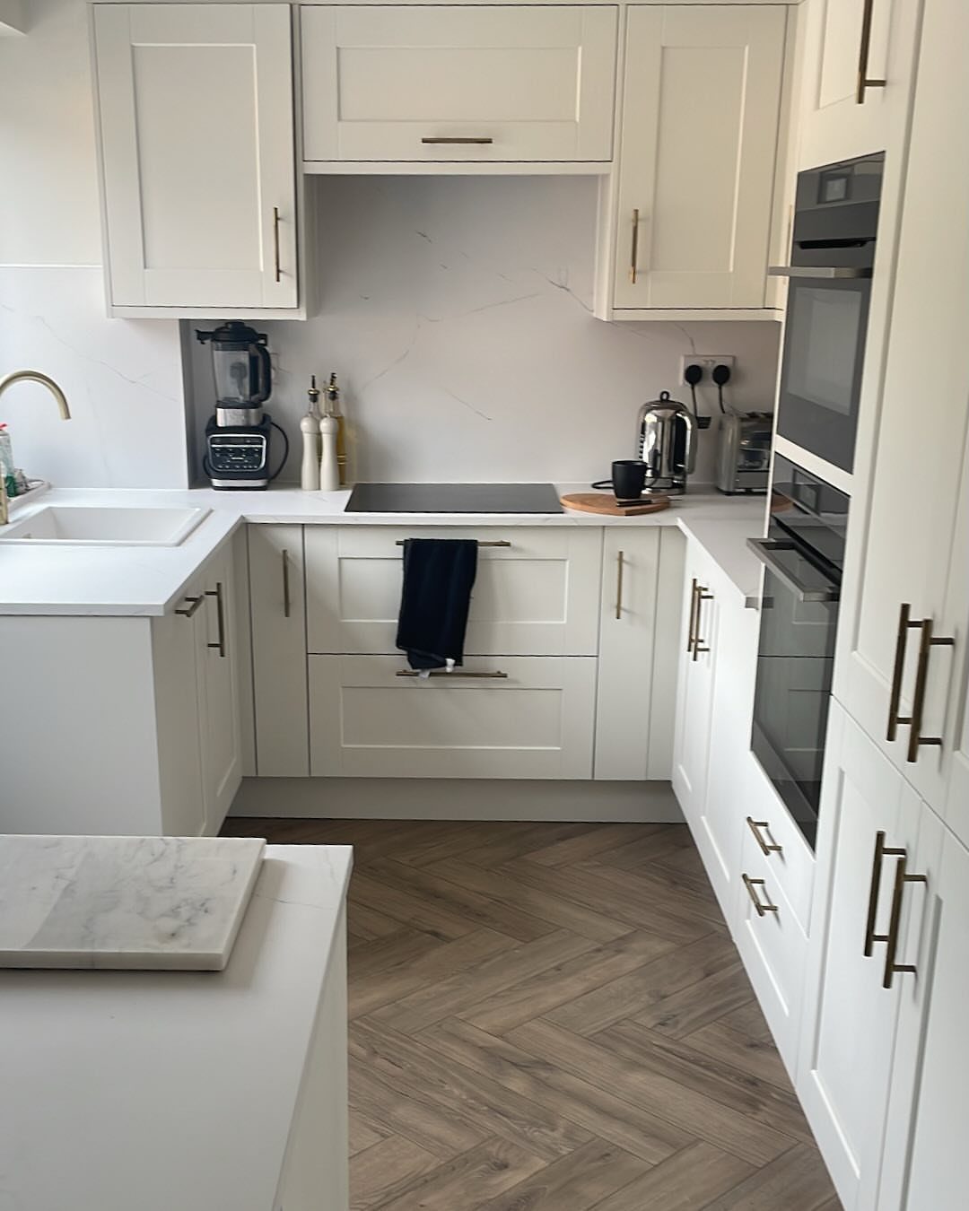 White Shaker cabinets with dark handles in a bright kitchen with herringbone floors.