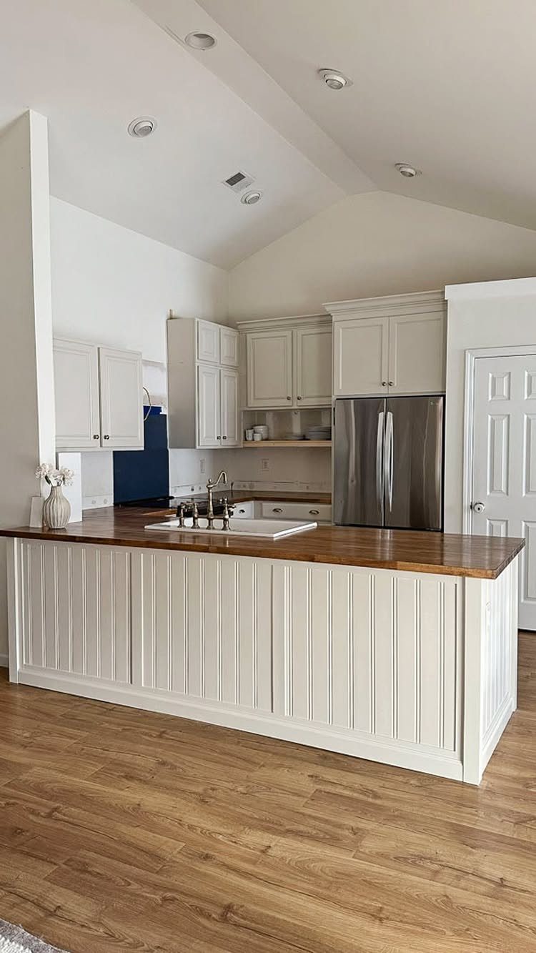 White kitchen island with a brown wood countertop and light wood flooring.