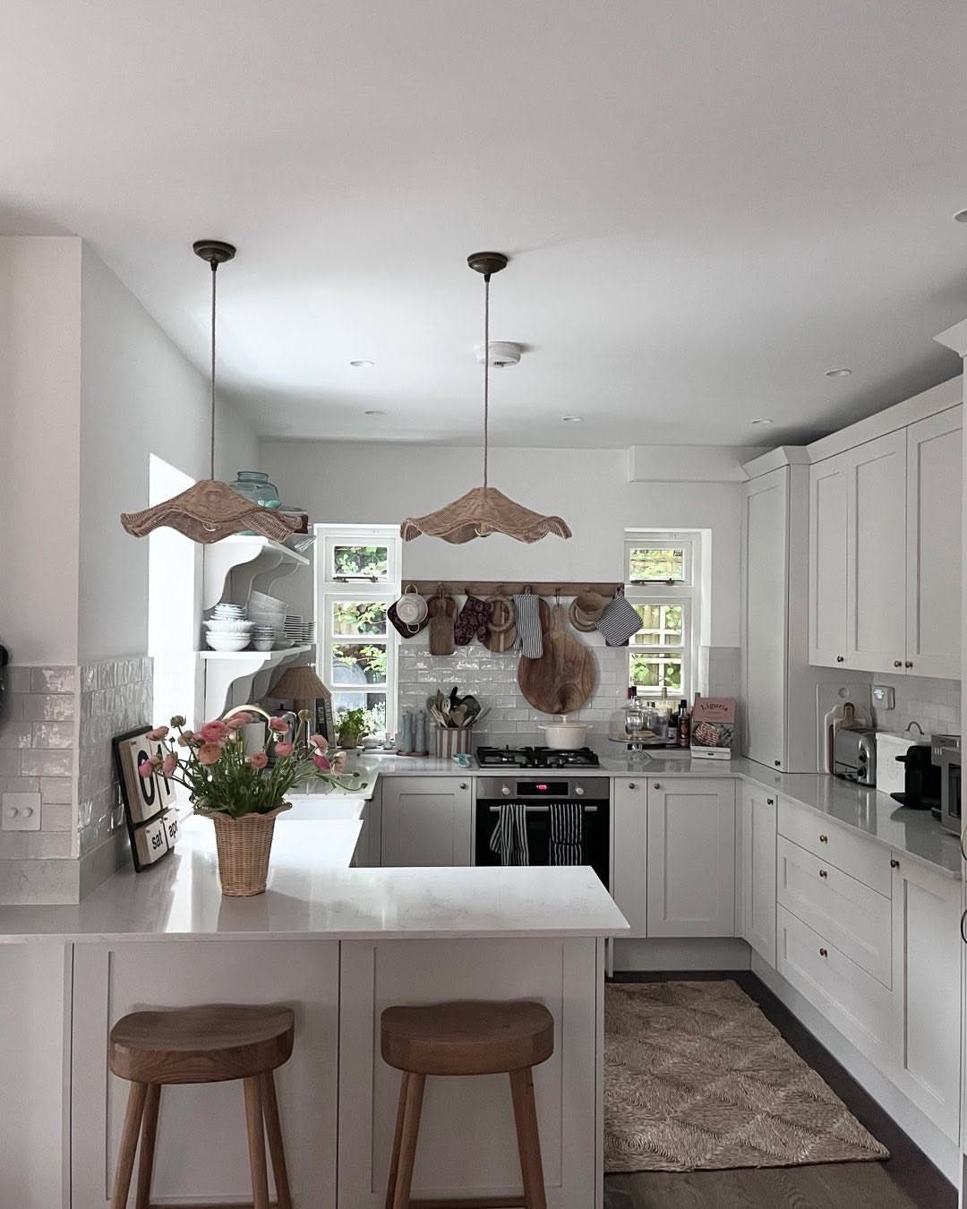 White kitchen with white cabinets, white countertops, and two wooden island stools.