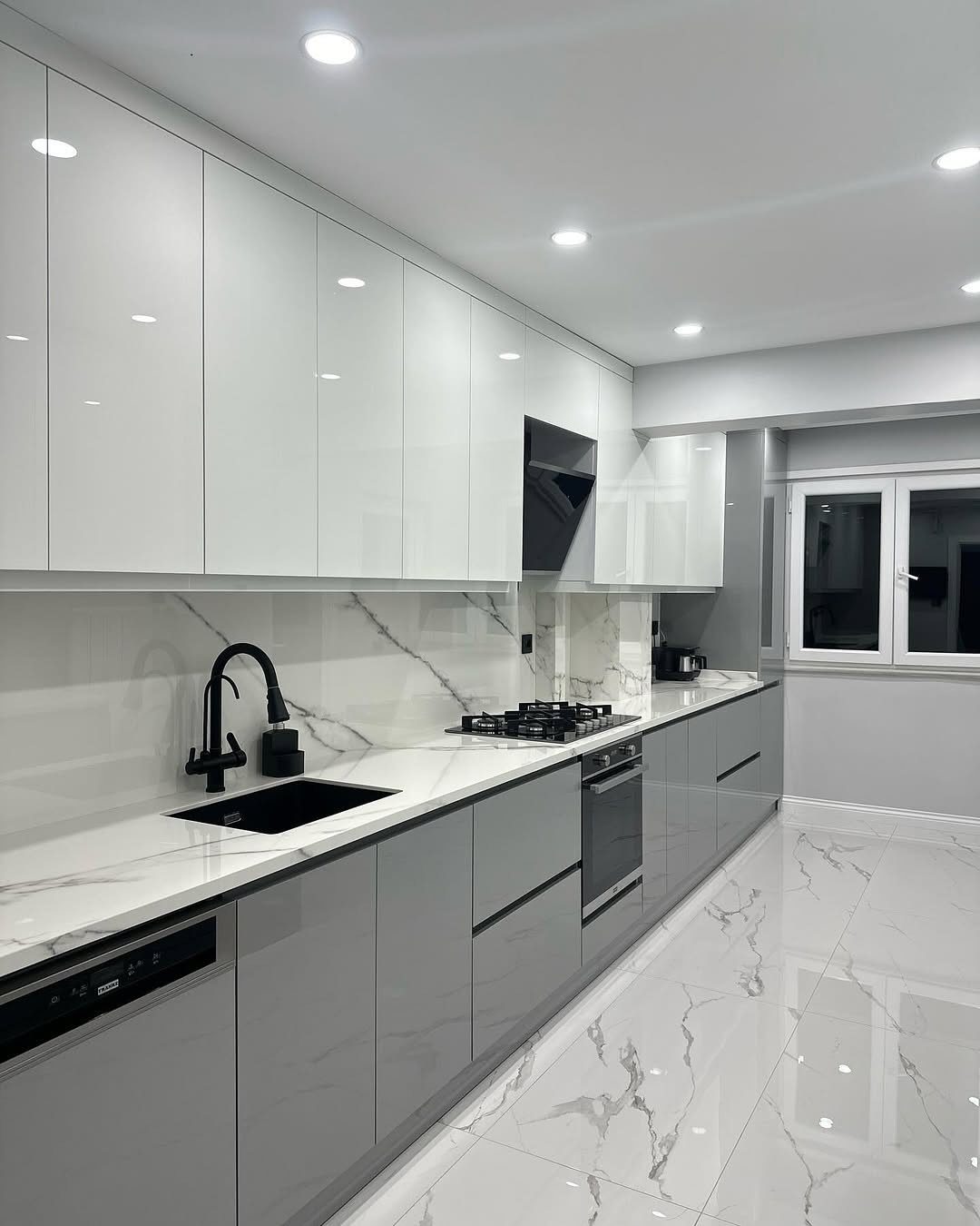 Modern kitchen with glossy white upper cabinets, gray lower cabinets, and marble flooring.