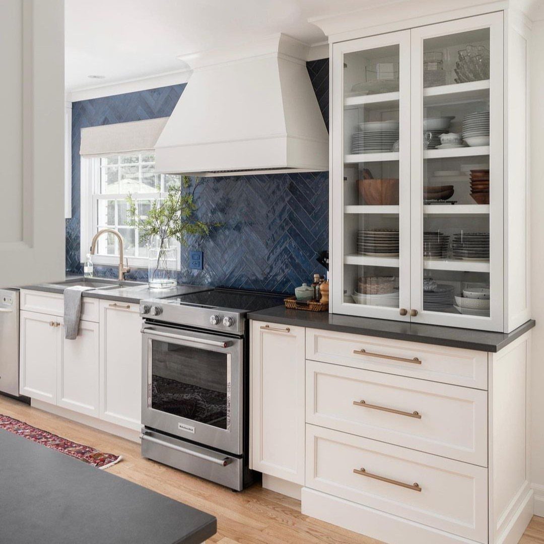 White shaker cabinets and a deep blue herringbone tile backsplash in a modern kitchen.