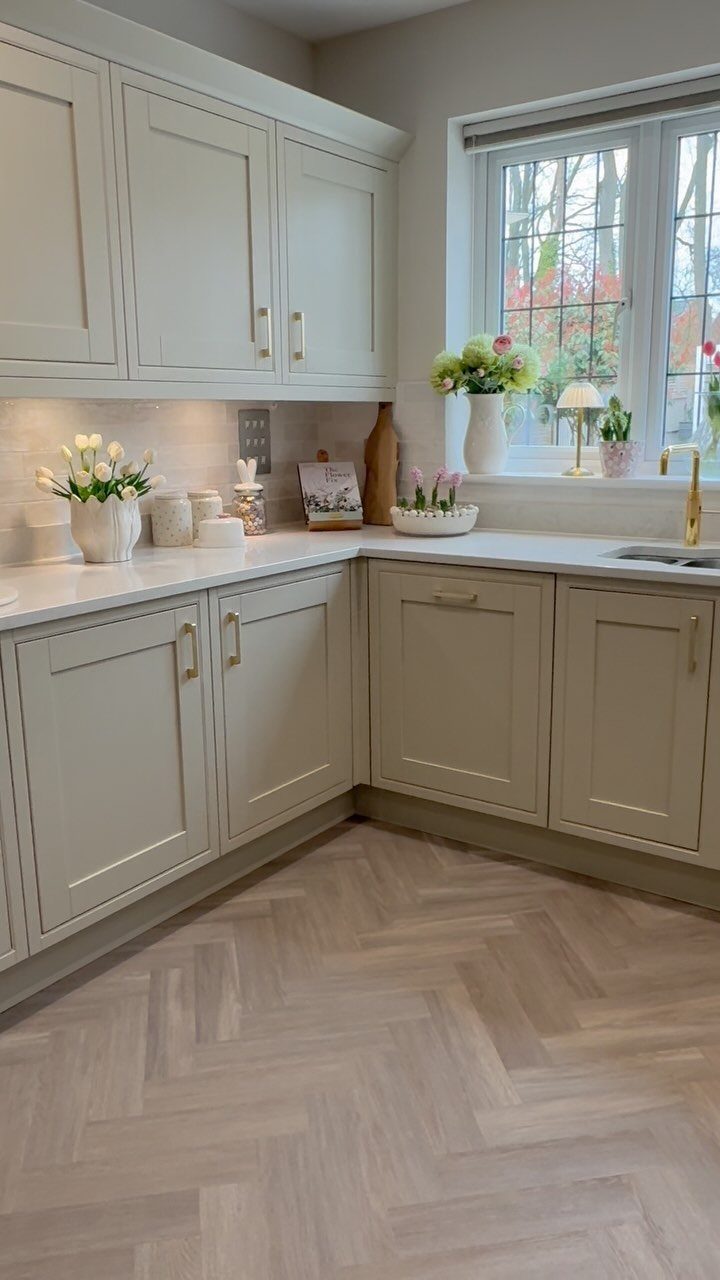 White shaker cabinets with gold hardware and light herringbone wood flooring in a kitchen.