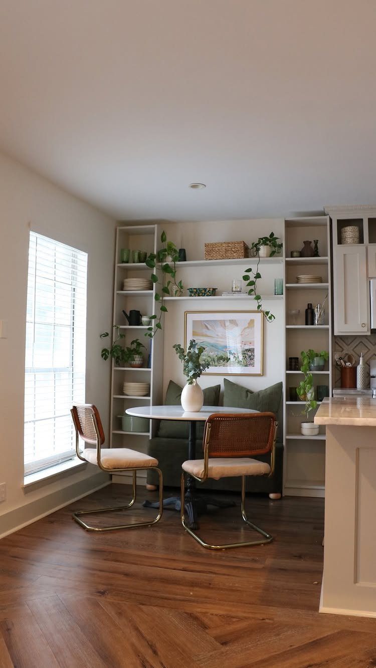 Dining nook with round white table, green banquette, and white built-in shelving.