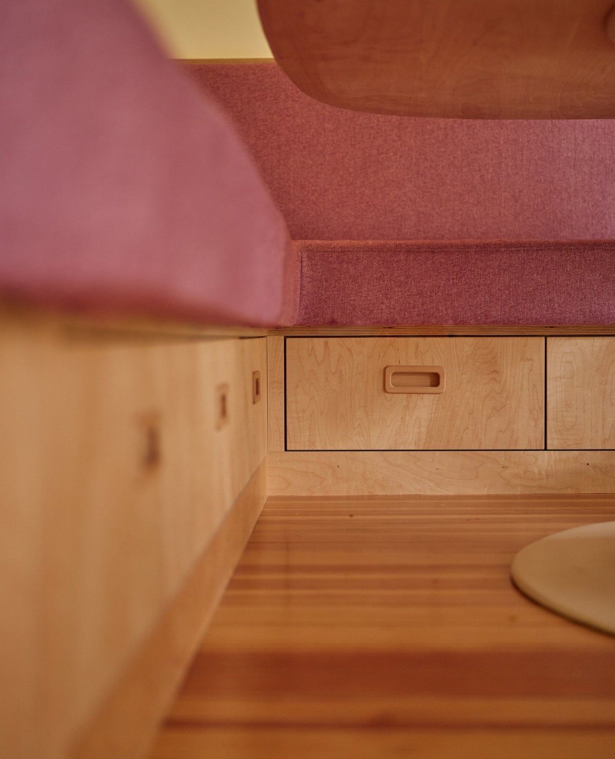 Wooden kitchen nook with pink upholstery and built-in storage drawers underneath the seat.