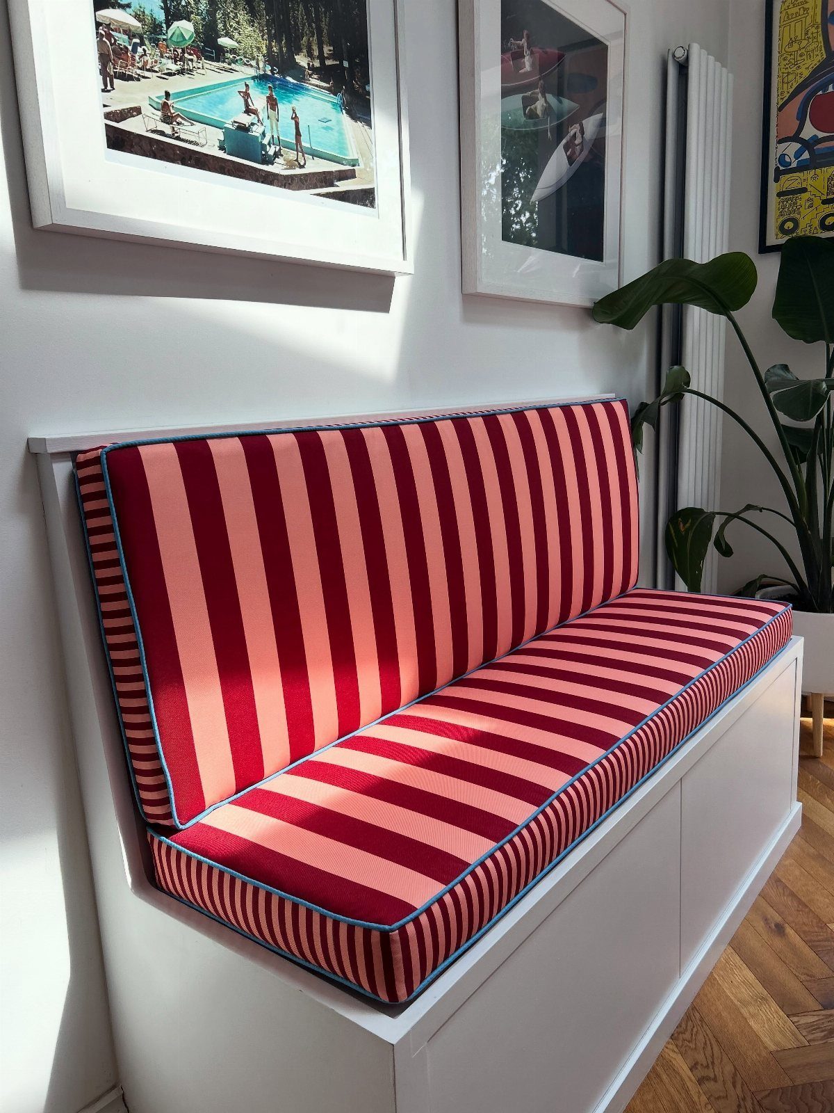 White built-in storage bench with red and pink striped cushions against a wall.