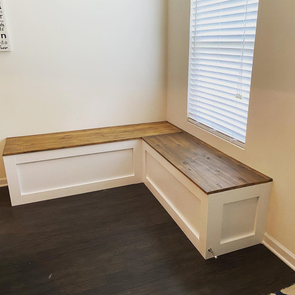 L-shaped white built-in kitchen bench with a natural wood top and dark flooring.