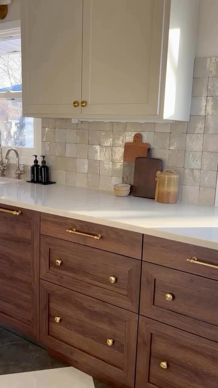 12 Kitchen Updates on a Budget, From Hardware to Pantry Jars 1 Dark wood kitchen cabinets with gold hardware and white countertops against a tiled backsplash.