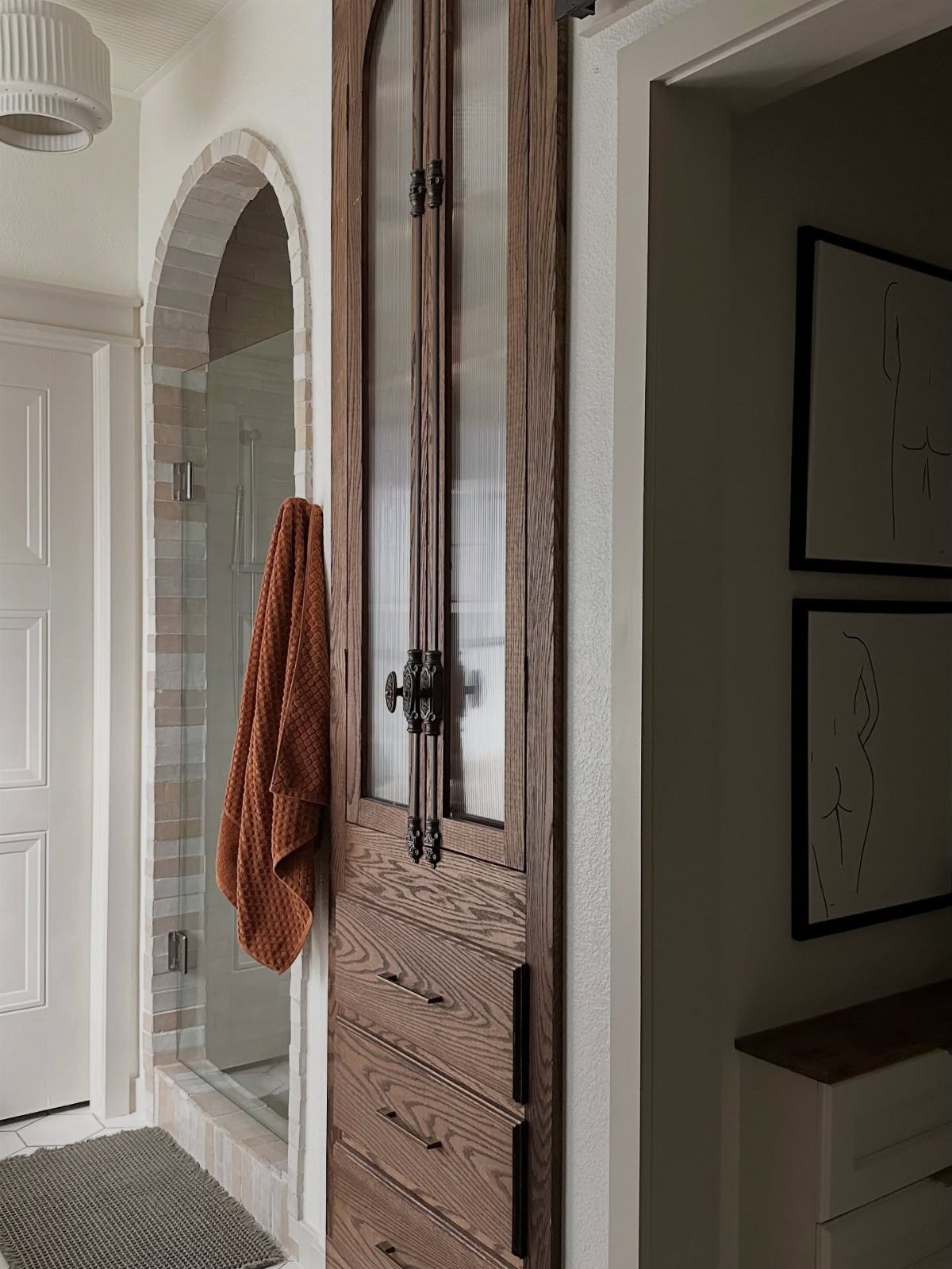 Wooden sliding door and arched entryway leading into a modern tiled bathroom shower