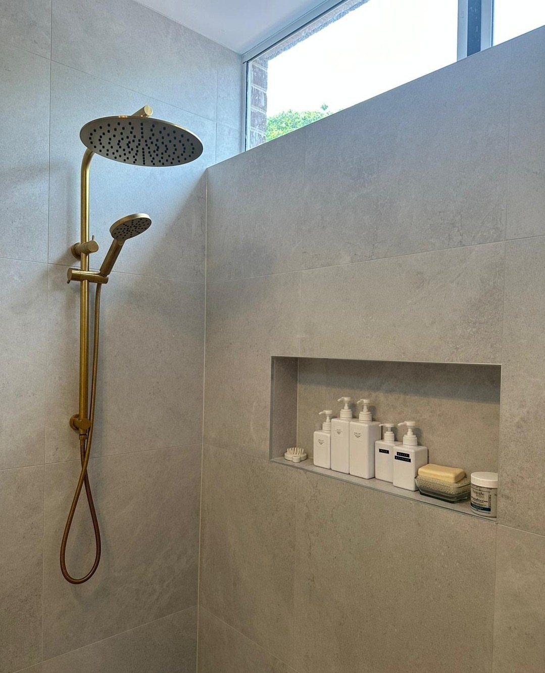 Recessed shower niche with white bottles built into a grey tiled bathroom wall.