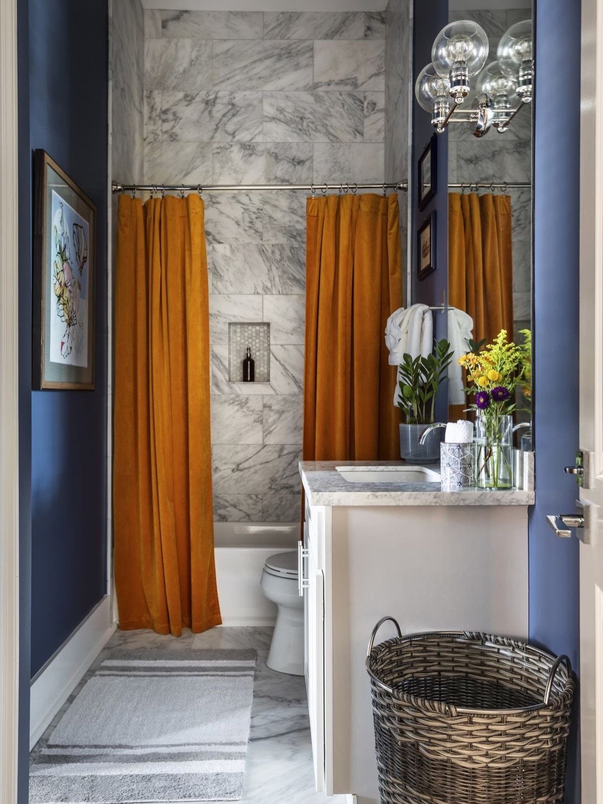 Modern bathroom with white marble walls, mustard yellow shower curtains, and deep blue walls.