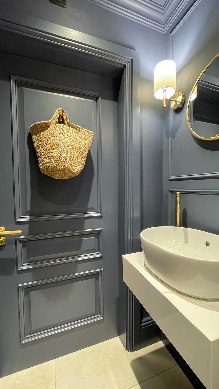 Modern bathroom with dark blue paneled walls, white vessel sink, and gold accents.