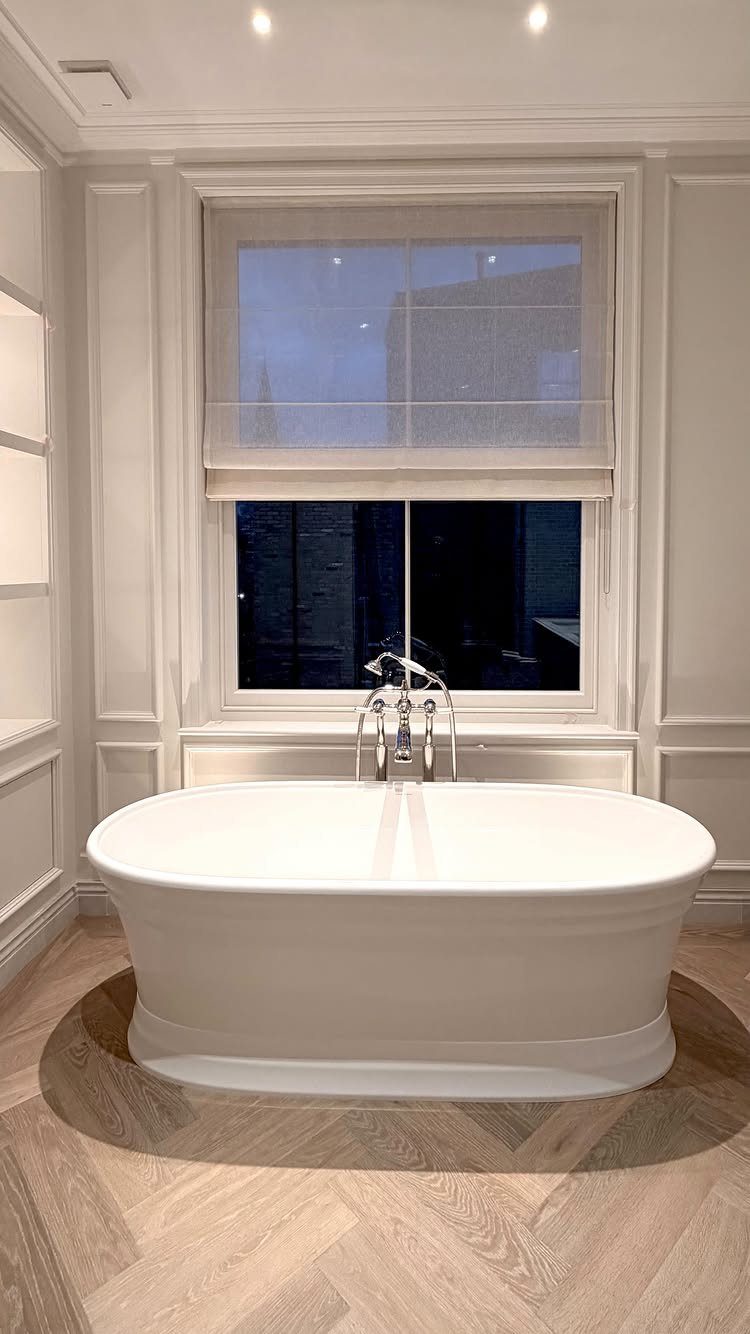 White freestanding bathtub in a bright bathroom with paneled walls and herringbone floors.