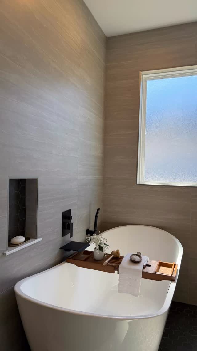 White freestanding bathtub with a wooden tray and flowers against grey textured walls.