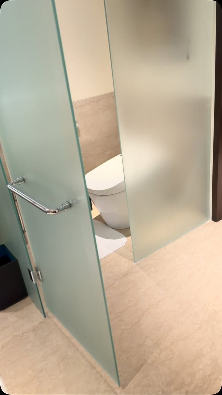 White toilet partially hidden behind frosted glass partitions in a modern bathroom.