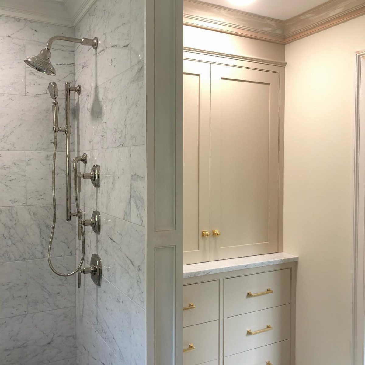 Built-in cream linen cabinet with gold hardware next to a marble shower.