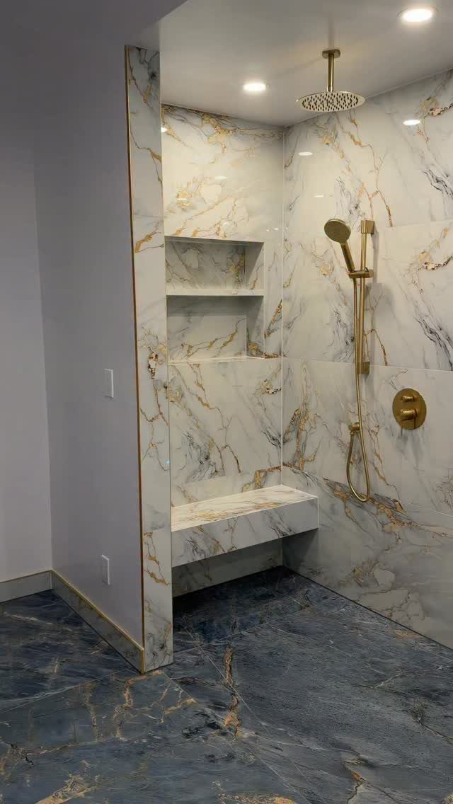 Walk-in shower with large white marble wall tiles and dark blue marble flooring.
