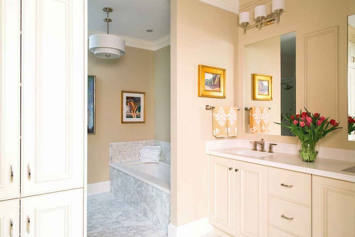 White double vanity and marble bathtub in a bright, luxury bathroom with marble floors.