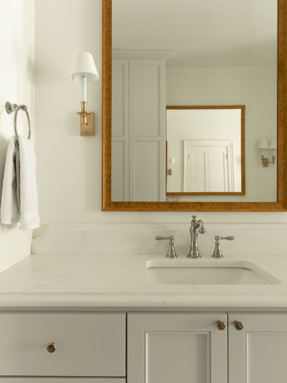 White bathroom vanity with chrome faucets and gold hardware and lighting fixtures.