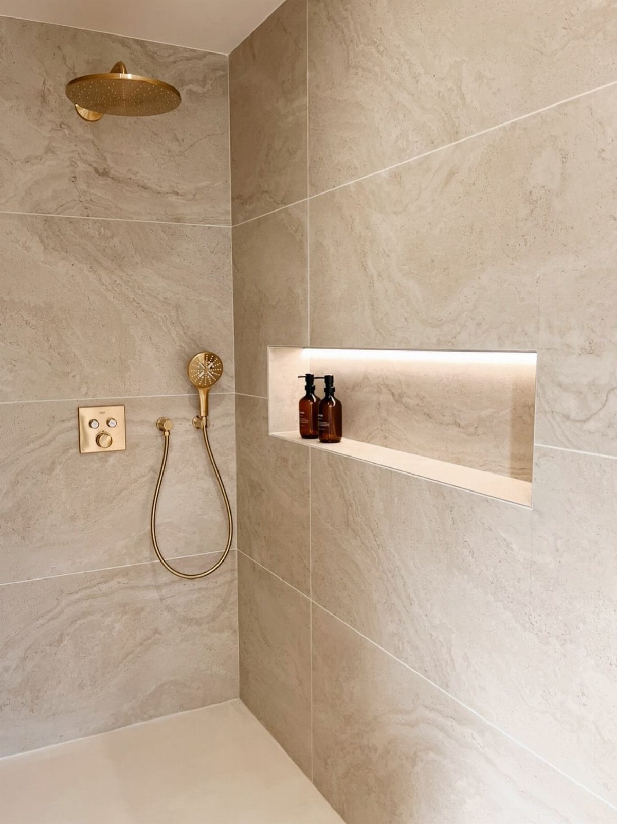 Beige marble stone feature wall in a shower with gold fixtures and illuminated niche