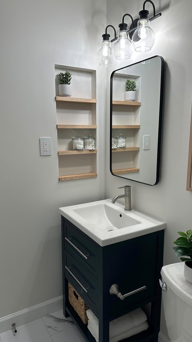 Dark blue bathroom vanity with a white sink and recessed wooden wall shelving.