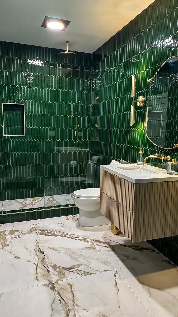 Modern bathroom with green tiled walls, white marble floors, and a wooden vanity.