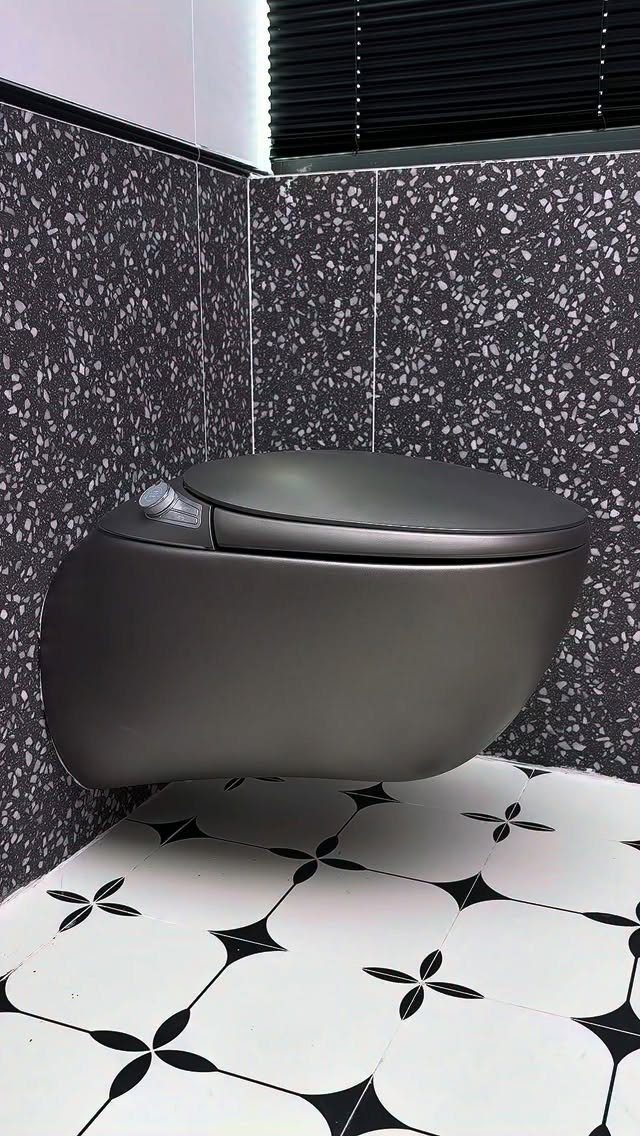 Matte black wall-hung toilet in a bathroom with dark terrazzo walls and patterned flooring.