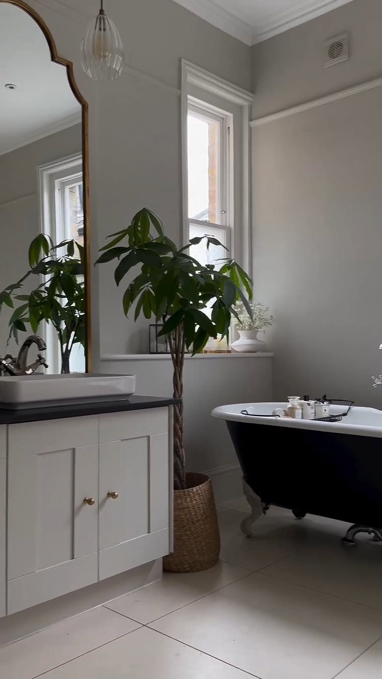White bathroom vanity and black clawfoot tub against warm white walls with a plant.