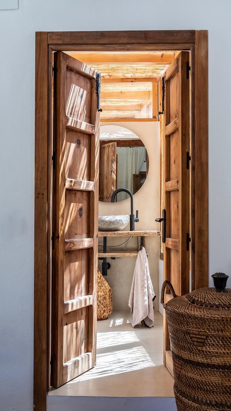Wooden doors opening into a bathroom with a stone sink and round mirror.