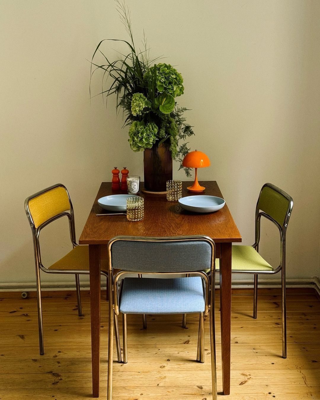 Mismatched Chairs Dining Table: 12 Ideas for a Cohesive Look 9 Wooden dining table with yellow, blue, and green mismatched chairs and green flowers.
