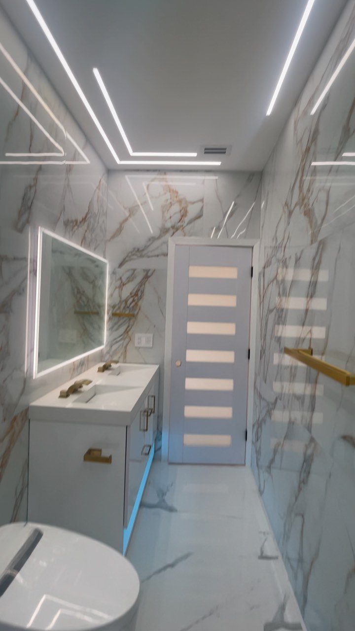 12 Mobile Home Master Bath Remodel Ideas and Moisture Tips 3 Backlit rectangular mirror above a white vanity in a marble-walled modern bathroom.