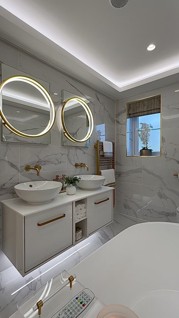 12 Mobile Home Master Bath Remodel Ideas and Moisture Tips 6 Modern bathroom with white marble tiles, floating vanity, vessel sinks, and circular backlit mirrors.