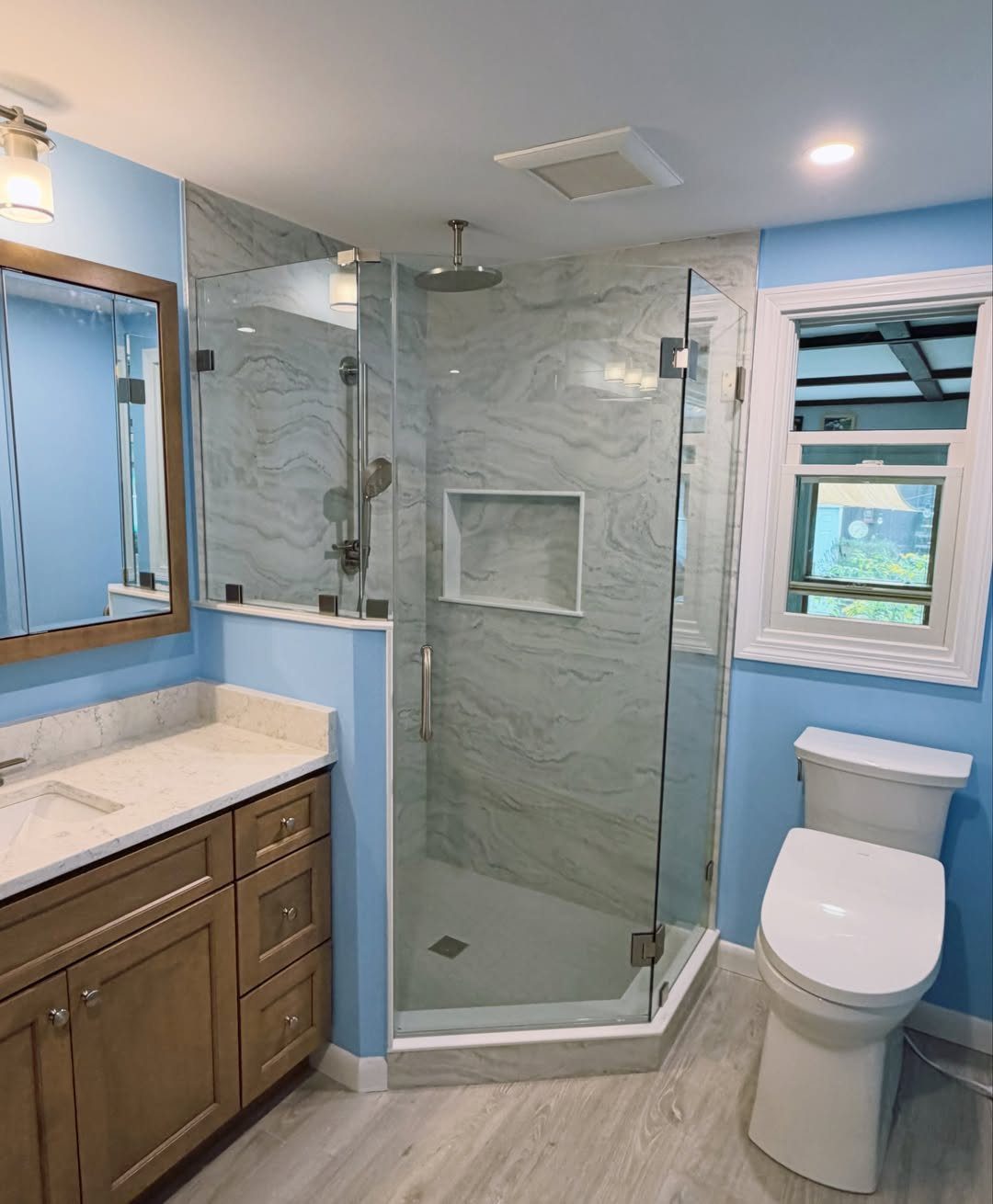 12 Mobile Home Master Bath Remodel Ideas and Moisture Tips 7 Neo-angle glass shower with marble walls in a blue bathroom with wooden vanity.