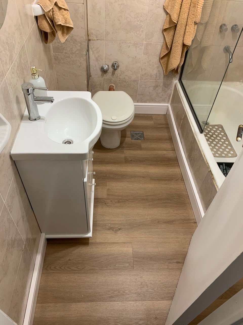 12 Mobile Home Master Bath Remodel Ideas and Moisture Tips 1 Brown wood-look vinyl plank flooring in a small bathroom with white fixtures.
