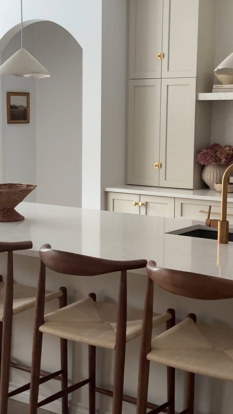 Neutral Kitchen Cabinets: 16 Colors From Greige to Black 8 Cream-colored kitchen cabinets with gold hardware and wooden bar stools in a bright room.