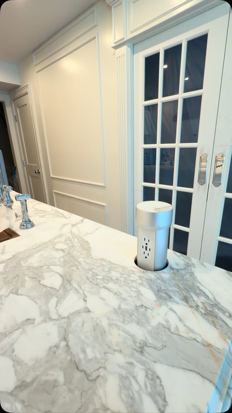 Silver pop-up electrical outlet installed in a white marble kitchen island countertop.