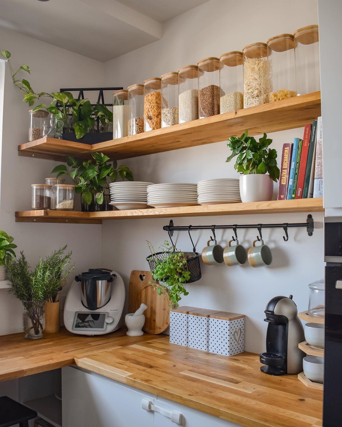 Wooden open shelves holding glass jars and plates in a bright white kitchen.