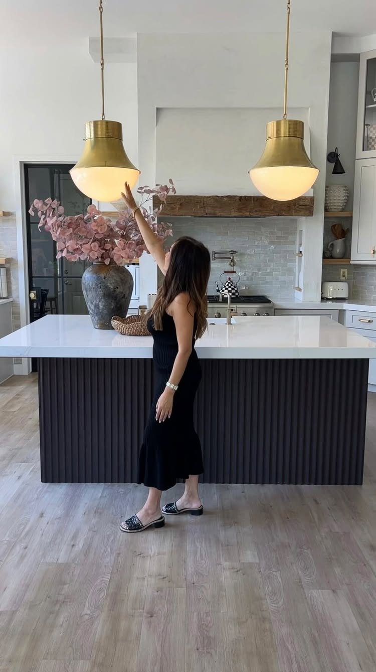 Two large gold pendant lights hanging over a white kitchen island with a woman.
