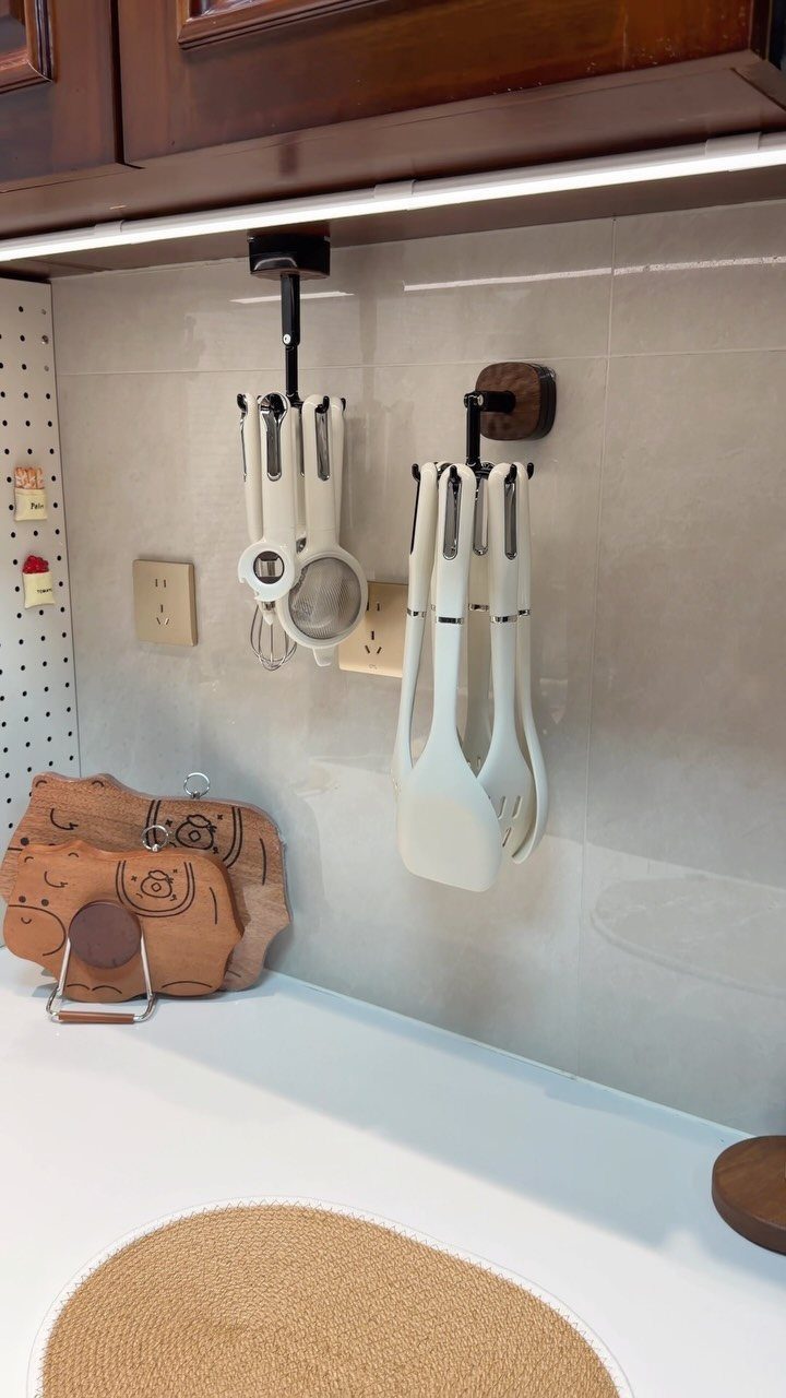 White cooking utensils hanging from black wall mounts against a tiled kitchen backsplash.