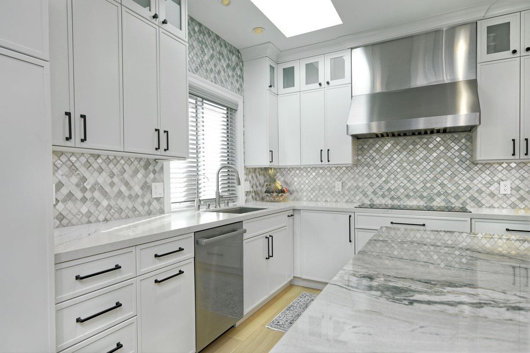 White kitchen with grey tile backsplash, stainless steel sink, and marble island countertop.