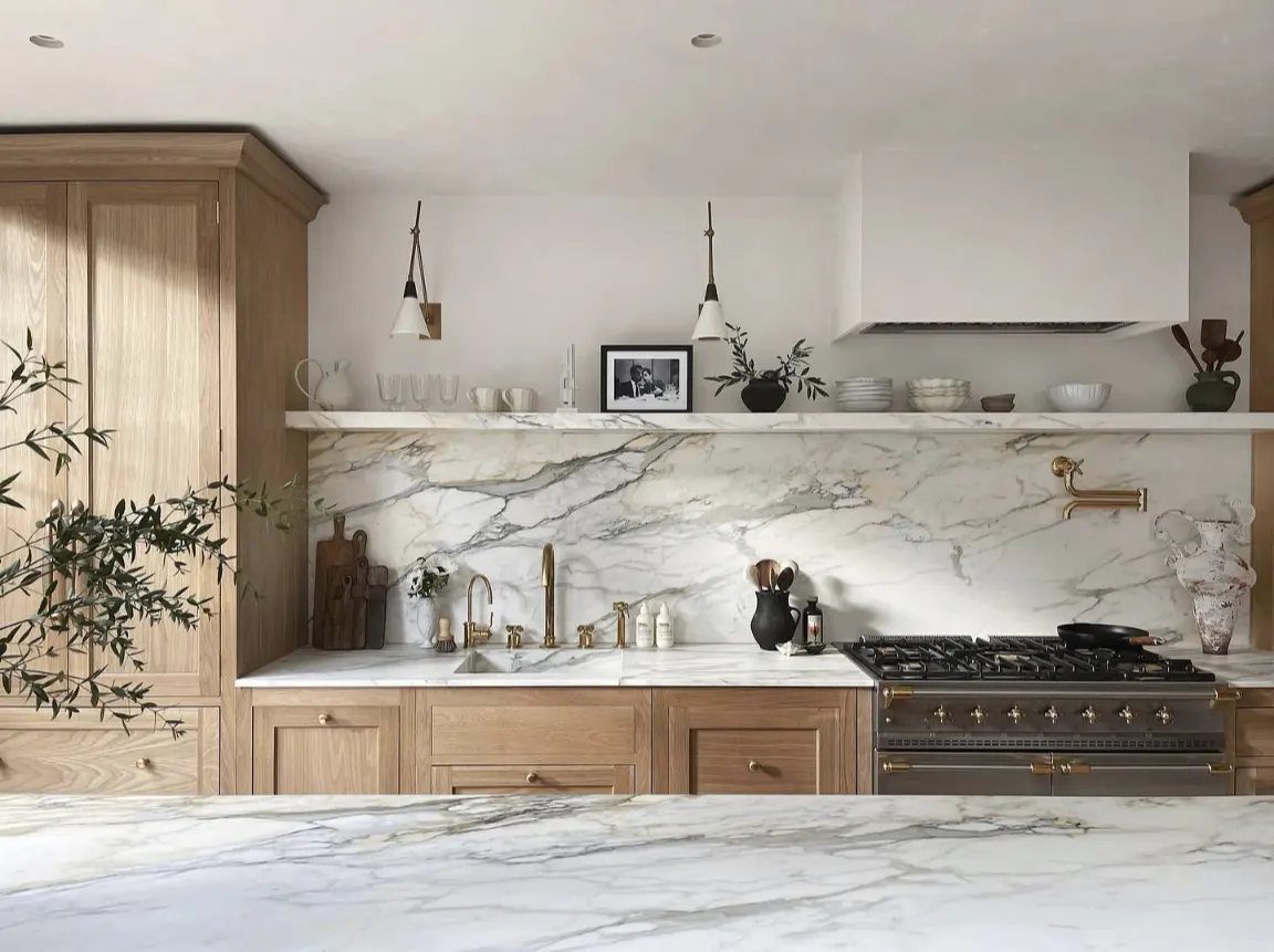 Light wood kitchen with white marble countertops, backsplash, and a professional gas range.