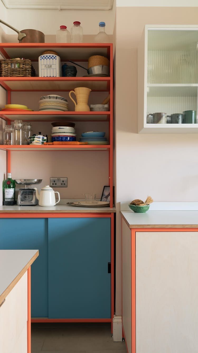 Orange open shelving and blue cabinets in a modern, colorful kitchen setting.