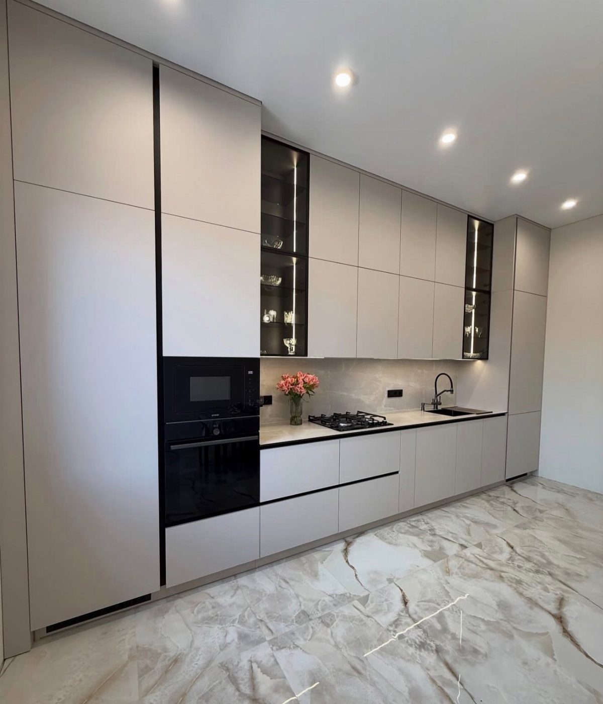 Modern one-wall kitchen with light grey cabinetry and white marbled tile flooring.