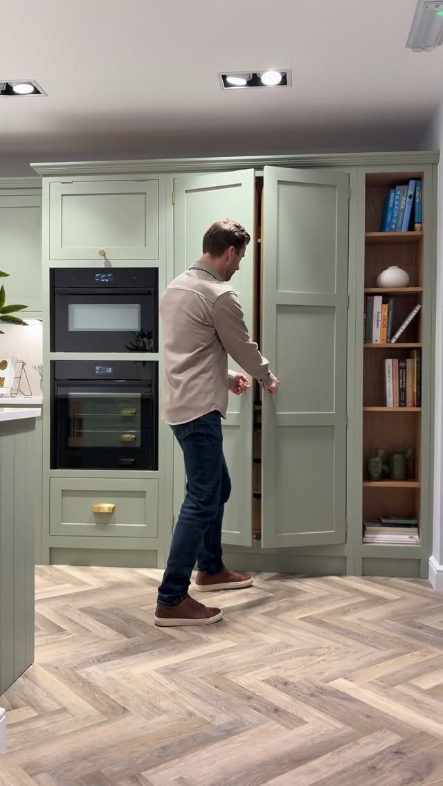 Man opening a tall sage green pantry cabinet in a modern kitchen setting.