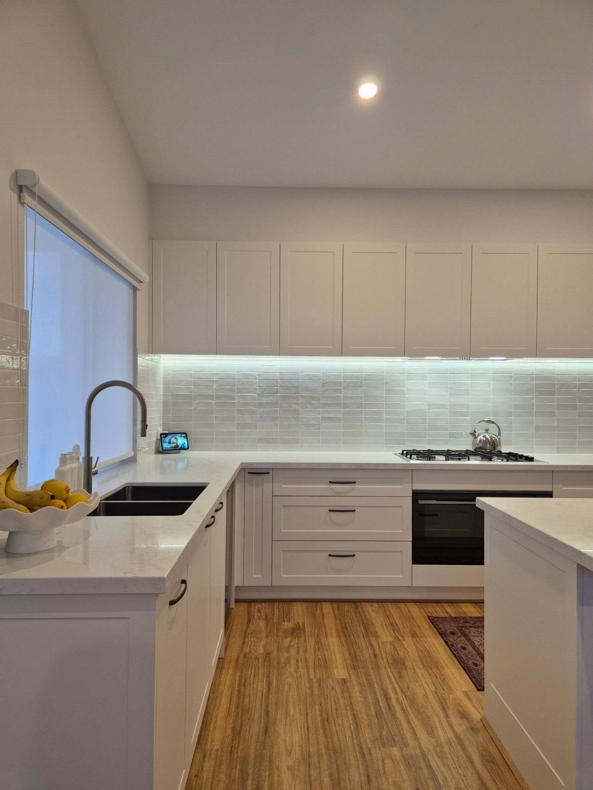 White shaker cabinets and white countertops in a bright, modern kitchen with wood floors.